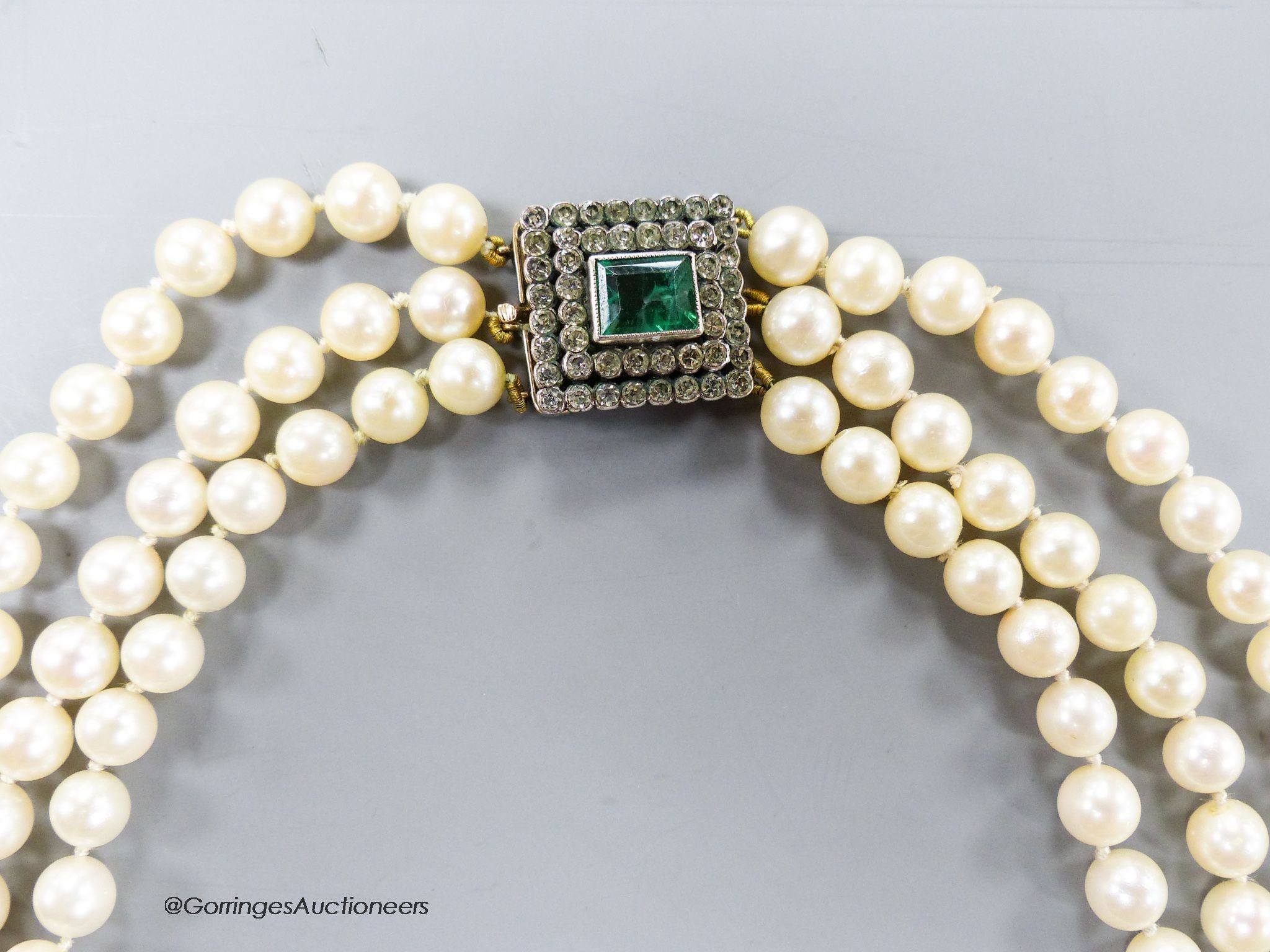 A triple strand cultured pearl set choker necklace, with two colour paste set yellow metal clasp, 42cm.